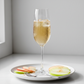 Fotografía realista de un vaso de champaña con jugo de manzana con burbujas finas y hielos, con rodajas de manzana alrededor. Estilo saludable y gourmet francés, iluminación natural suave, fondo claro minimalista, sin texto ni personas. Formato cuadrado.